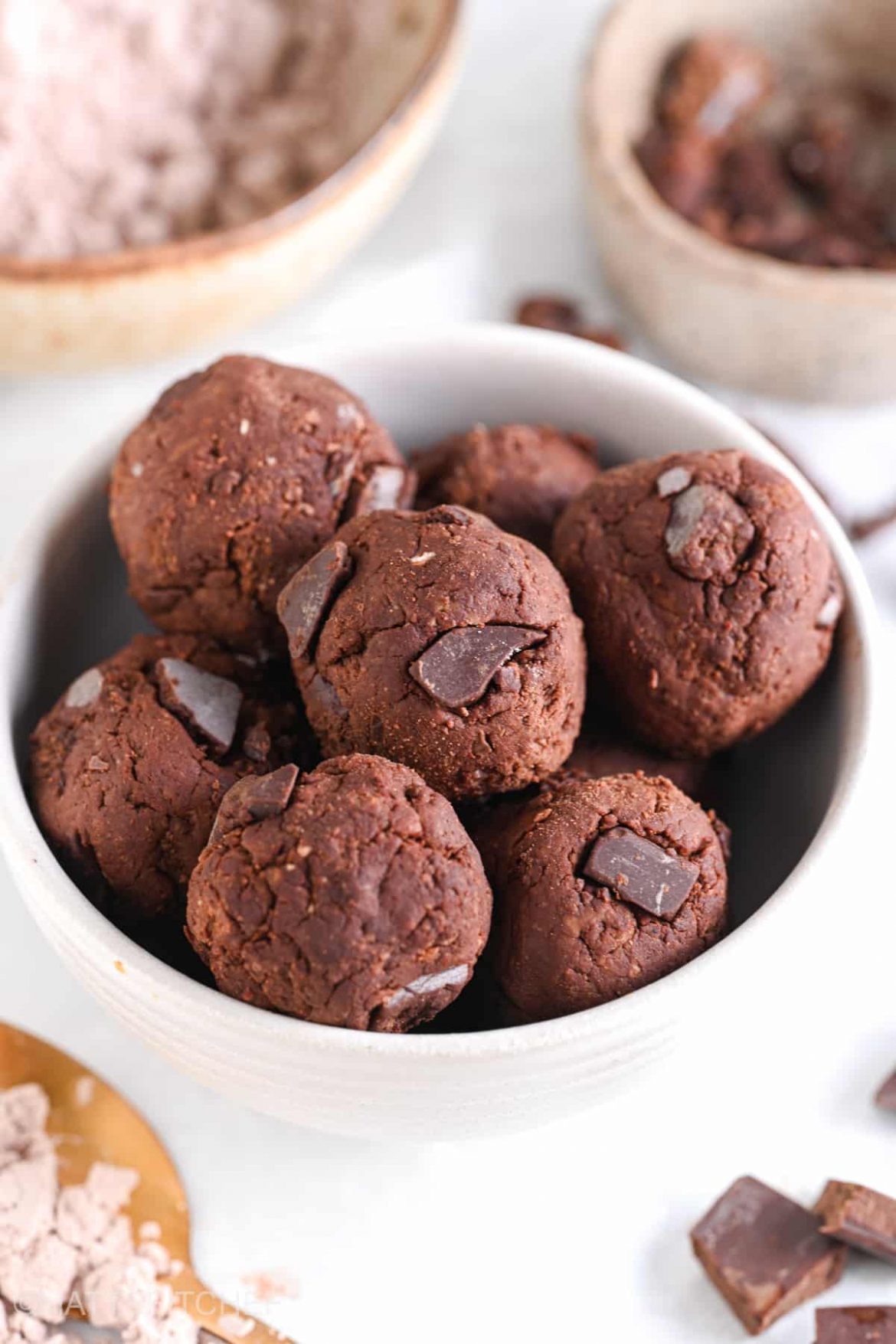 Close-up of protein brownie bites with chocolate protein powder and chocolate chunks in the background