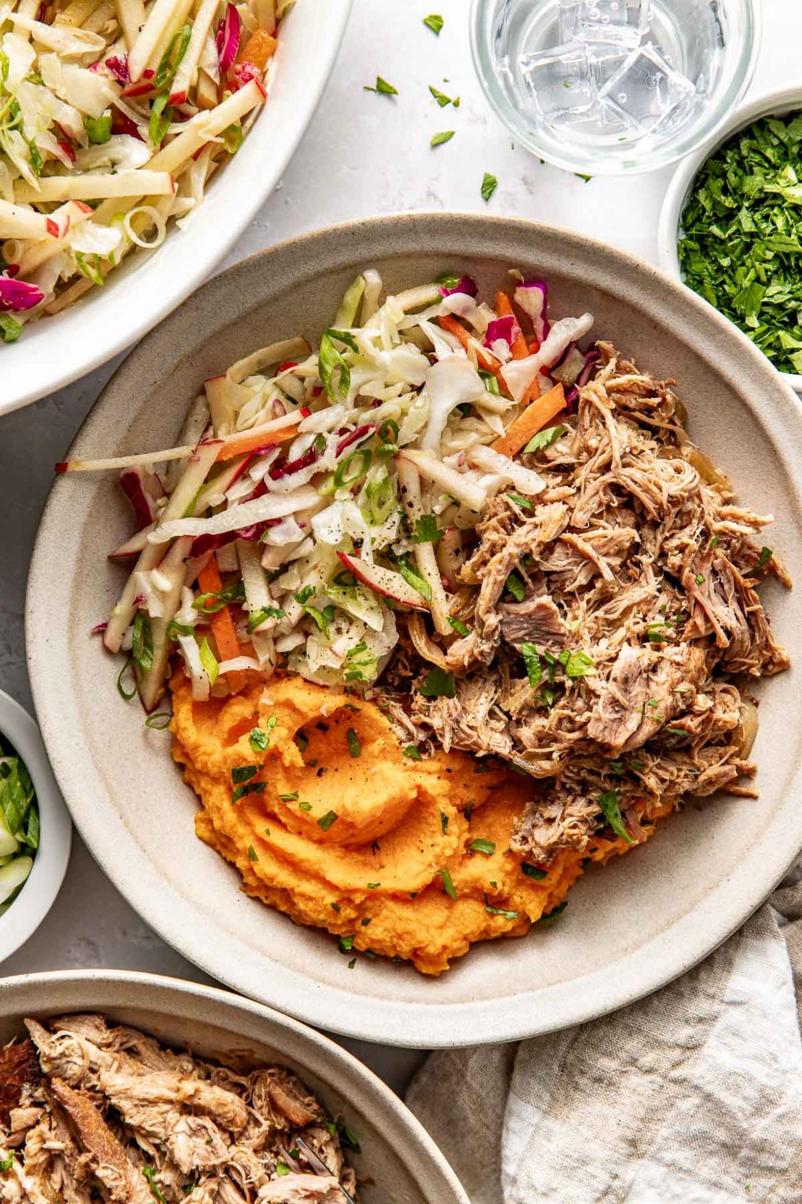 Overhead view of a white bowl filled with deep orange mashed sweet potatoes, pulled pork, and colorful fresh apple slaw. 