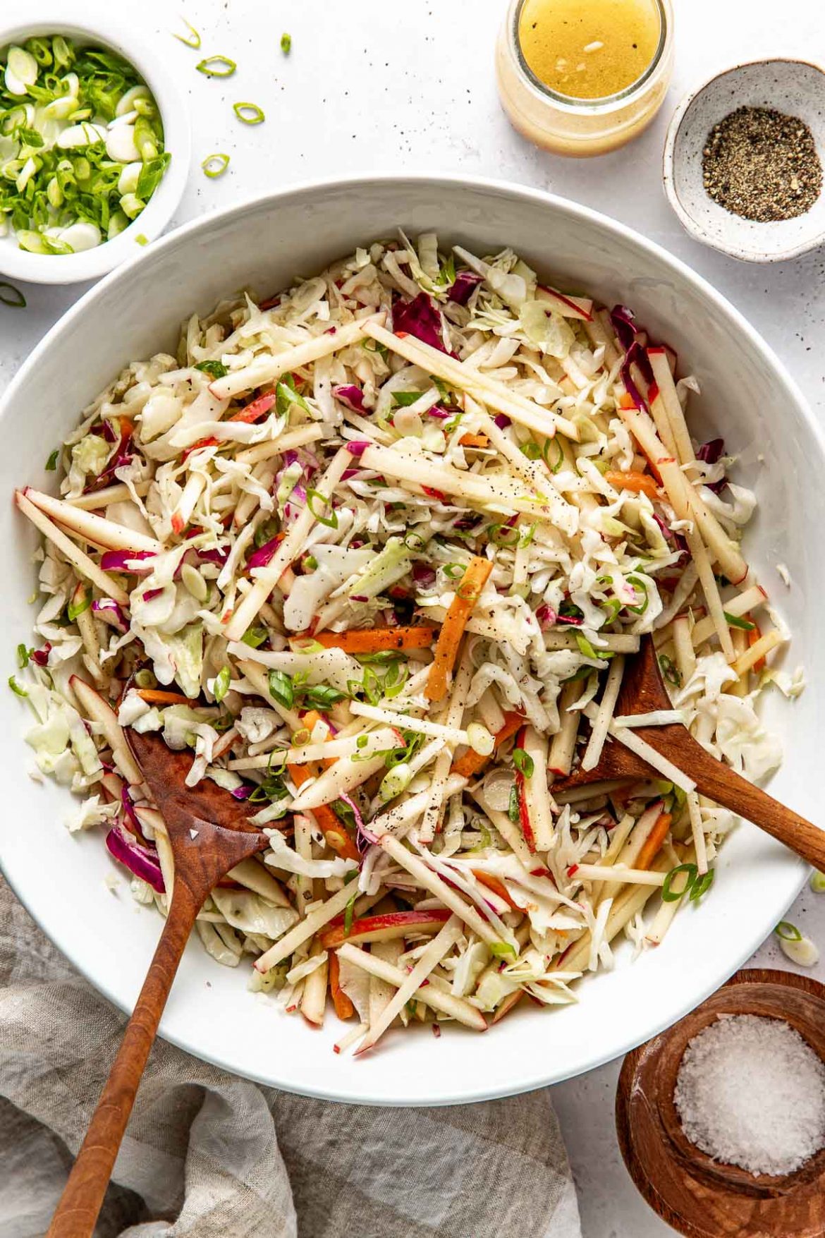 Overhead view of a white bowl filled with colorful Apple Slaw topped with black pepper and green onions. 