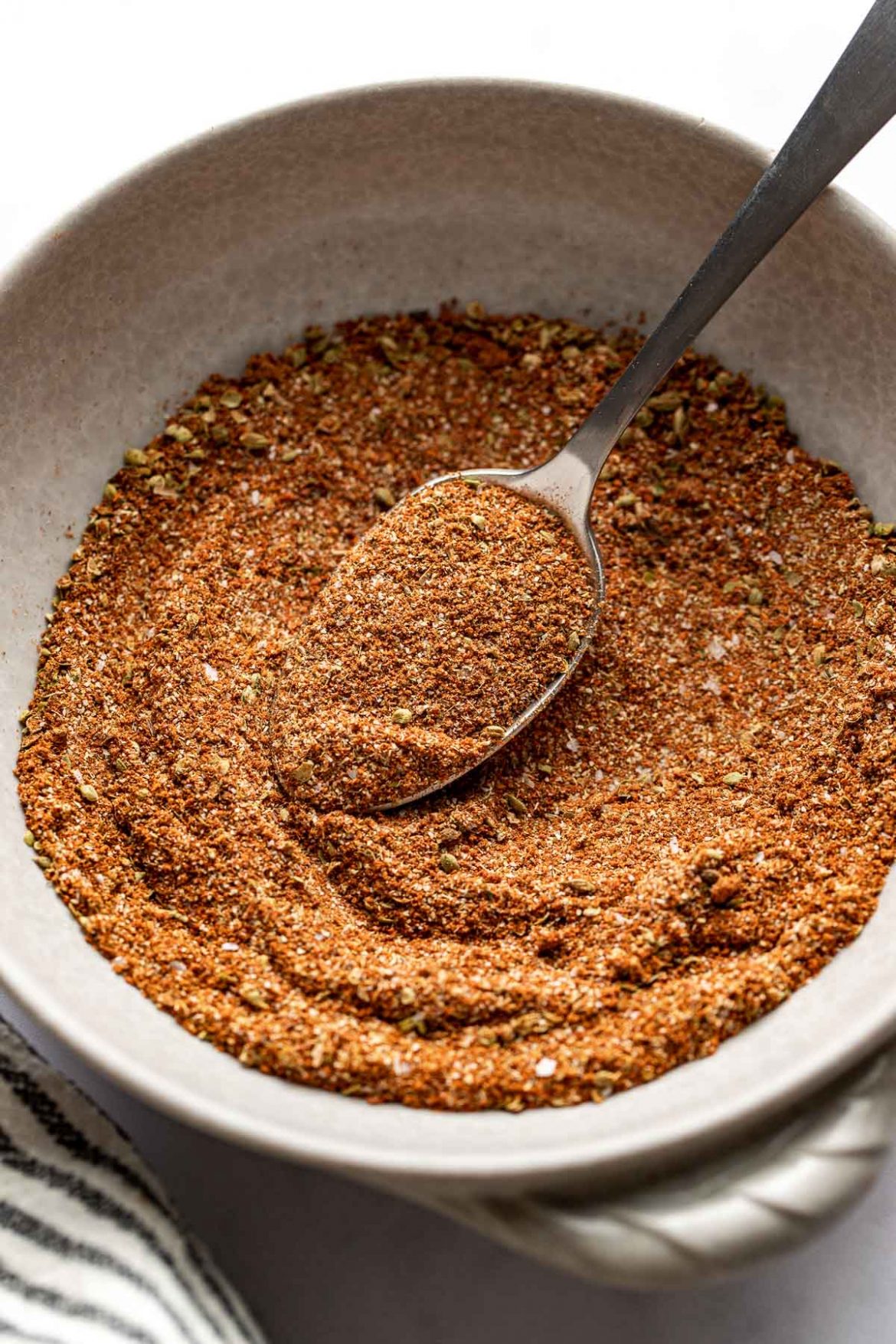 Close up view of a ceramic bowl filled with Homemade Taco Seasoning and a spoon in the bowl. 
