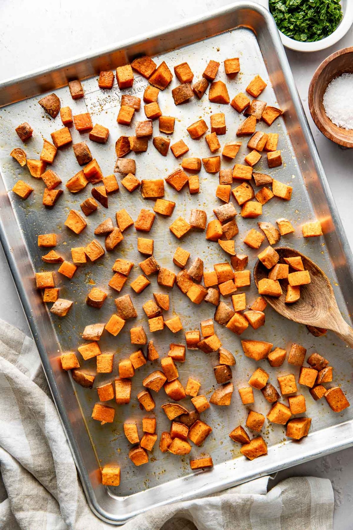 Overhead view of a metal sheet pan filled with freshly Roasted Sweet Potatoes topped with seasonings and crisp on the edges. 